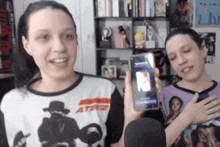 a woman wearing a shirt that says ' ateez ' on it holds up a cell phone