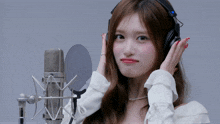 a woman wearing headphones and a white shirt stands in front of a microphone