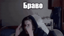 a man in a hoodie is sitting on a bed covering his face with his hand .