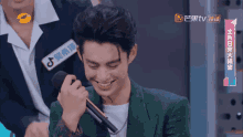 a man in a green jacket is smiling while holding a microphone in front of a sign that says tv