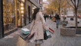 a woman walking down a sidewalk carrying a bunch of shopping bags including one that says ' gucci ' on it