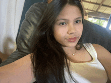 a woman with long black hair is wearing a white tank top and pearl necklace
