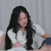 a woman with long black hair is sitting on a couch with her eyes closed and looking down .