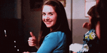 a woman is smiling and giving a thumbs up sign while sitting at a table .