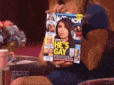 a woman is holding a magazine that says " he 's gay "