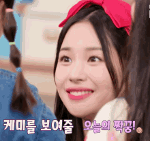 a girl with a red bow on her head is smiling with korean writing behind her