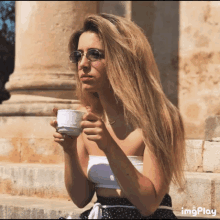 a woman wearing sunglasses holds a cup of coffee in her hand
