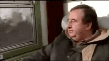 a man is sitting on a train looking out a window .