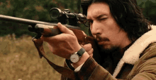 a man with long hair and a beard is holding a rifle with a scope on it .