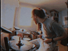 a man in a gray shirt is playing a set of drums