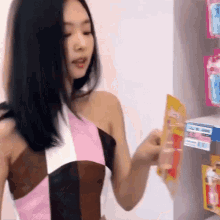 a woman in a pink and brown dress is standing in front of a shelf holding a packet of gum .