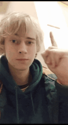 a young man in a blue hoodie is giving a middle finger