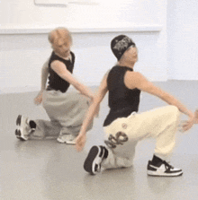 a man in a black tank top is squatting next to another man in white pants