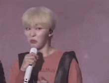 a young man is singing into a microphone while wearing a red shirt .