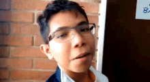 a young boy wearing glasses is making a face in front of a brick wall .