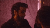 a man with a beard and ear piercings looks at another man