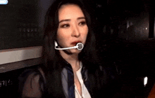 two women are standing next to each other in a dark room . one of the women is wearing a microphone .