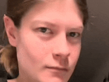 a close up of a woman 's face with a ponytail looking at the camera .