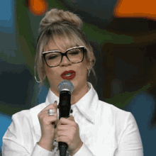 a woman wearing glasses holds a microphone in her hand