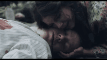 a woman kisses a man on the forehead who is laying on the ground