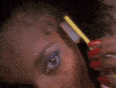 a woman with red nails is brushing her eyebrow with a yellow brush