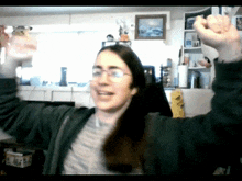 a woman wearing headphones and a green jacket holds her arms up in the air