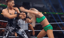 a woman in a green outfit is fighting a man in a black and white striped outfit in a wrestling ring