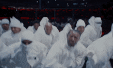 a group of people wearing white hooded clothes are running in a dark room