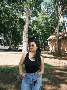 a woman wearing sunglasses and a black tank top stands in front of a thatched hut