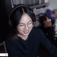 a woman wearing headphones and glasses is smiling in front of a microphone with a sticker that says $ 500