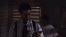 a man in a white shirt and black suspenders is sitting in front of a window in a dark room .
