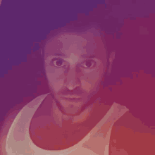 a man with a beard wearing a white tank top is making a funny face .
