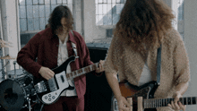 two men are playing guitars in front of a drum set in a room