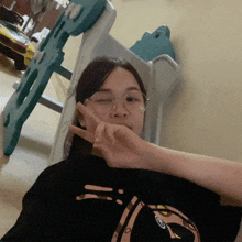 a woman wearing glasses and a black shirt with the letter g on it is giving a peace sign