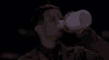 a man in a suit is drinking from a bottle in the dark .