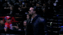 a man in a black leather jacket walks through a wrestling ring