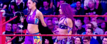 two female wrestlers are standing in a ring holding hands .