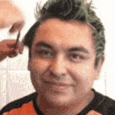 a man with green hair is getting his hair cut by a woman .