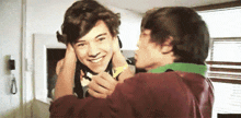 two young men are hugging each other in a room and one of them is putting his hand on the other 's neck .