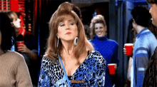 a woman in a blue and black leopard print shirt is standing in a crowd of people and saying bitchin .