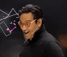 a man wearing glasses and a microphone stands in front of a blackboard with drawings on it