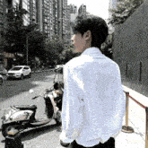 a man in a white shirt stands in front of a scooter on a street