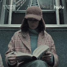 a woman is reading a book while wearing a hat with the words nine perfect strangers below her