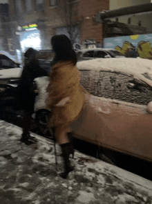 a woman walking in the snow next to a car that has snow on it