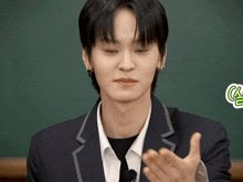 a young man in a suit and tie is clapping his hands in front of a green board