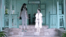 two women are standing on a set of stairs in front of a green house .