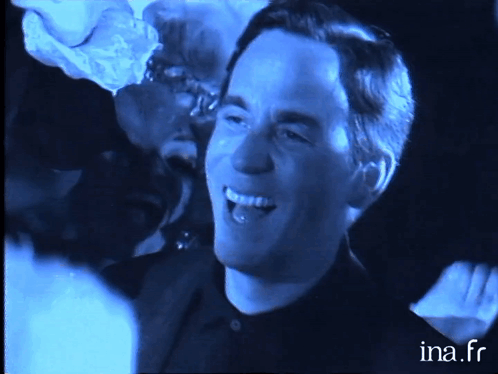 a man in a black shirt is smiling in a dark room with ina.fr written on the bottom