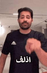 a man with a beard is wearing a black adidas t-shirt and making a funny face .