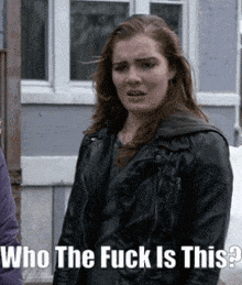 a woman in a leather jacket is standing in front of a building with the words " who the fuck is this " on the bottom