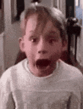 a young boy with his mouth open is wearing a white sweater .